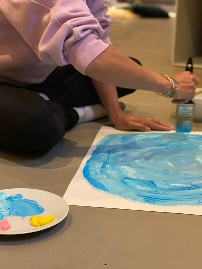 Een vrouw schildert geconcentreerd een blauwe cirkel op papier, met een schaaltje verf naast zich