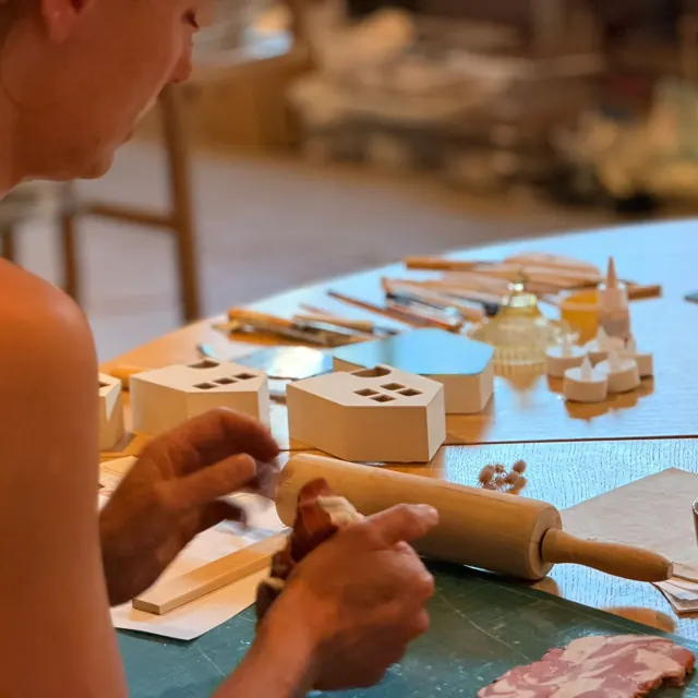 Handen die klei uitrollen met een deegroller, tussen zelfgemaakte huisjes