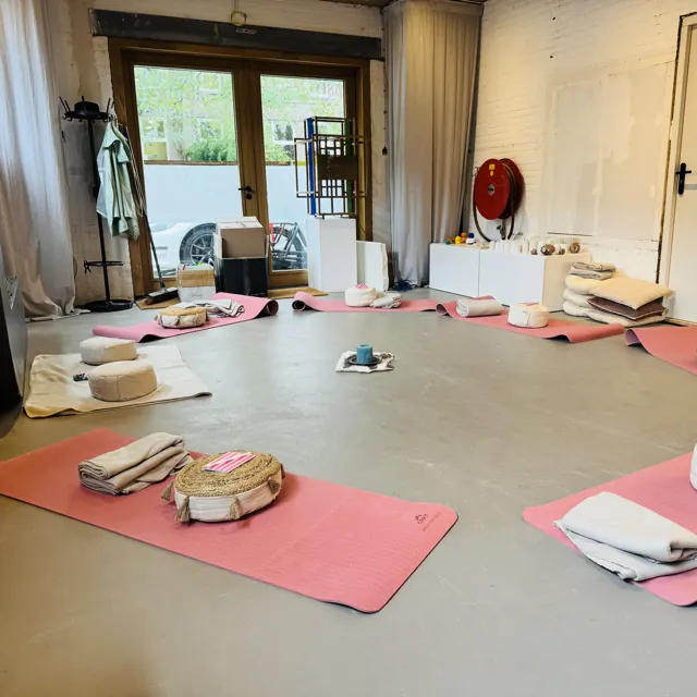 Yogamatjes in een kring klaargelegd voor de meditatie, met kussens en een kaars in het midden